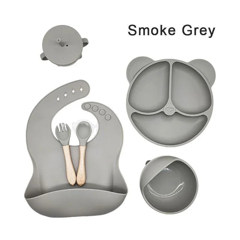 Set of smoke grey silicone utensils and plates on a white background