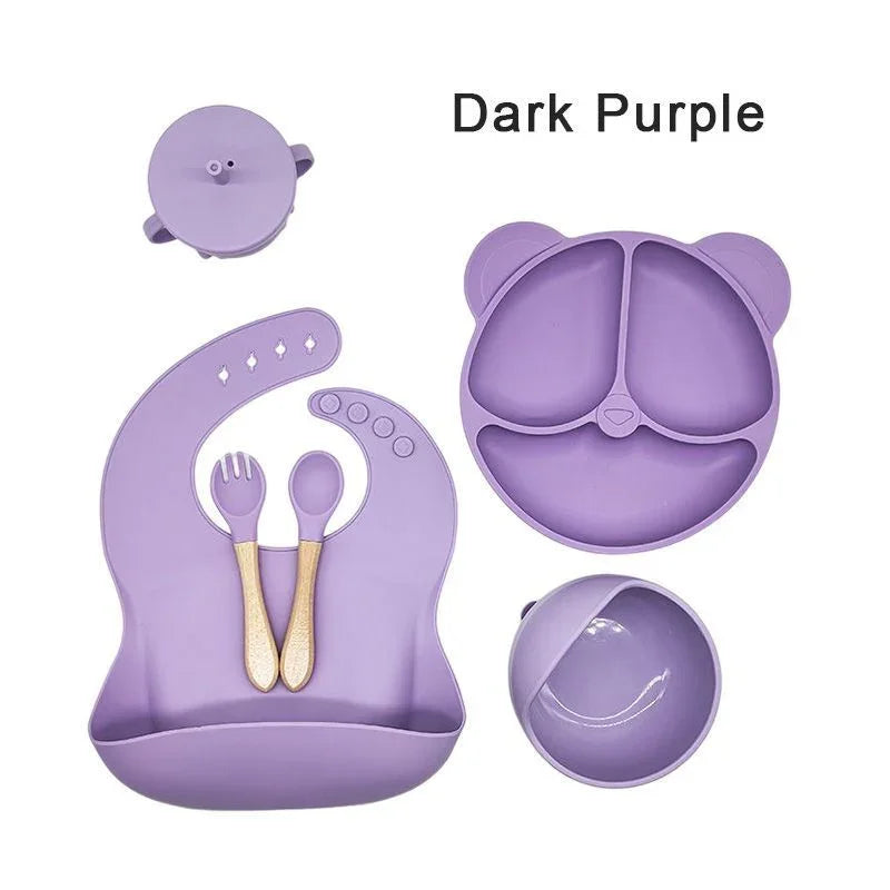Dark purple children's dining set with bowl, spoon, fork, and bib on a white background.